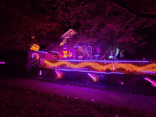 A West Seattle house with an orange pixel fence, purple light arches, glowing pumpkins, and ghosts beneath the trees